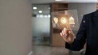 Businessman in suit touching glowing virtual screen with security shield and bank icons in modern office, digital finance protection concept.