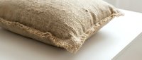 Rustic linen throw pillow with frayed edges resting on a white surface, showcasing natural texture and neutral beige tone for home decor.
