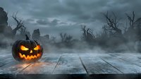 Glowing jack-o-lantern pumpkin on wooden deck with spooky graveyard background. Halloween horror scene with bare trees, tombstones and misty atmosphere.