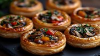 Savory mushroom tartlets with flaky pastry, topped with herbs and colorful vegetables, perfect for appetizers or party finger food.