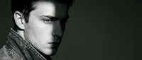Young handsome Caucasian man in leather jacket looking away pensively against dark background. Moody black and white portrait for fashion and lifestyle projects.