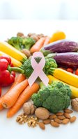 Pink ribbon with fresh vegetables and nuts promoting cancer awareness and healthy nutrition lifestyle on white background.