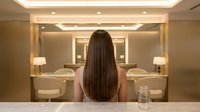 Woman with long brown hair looking at modern bathroom mirror with elegant lighting and contemporary design for spa and wellness concepts.