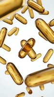 Golden vitamin capsules and softgels scattered on white background for health supplement and wellness product design applications.