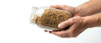 Caucasian male hands holding a glass jar filled with raw green lentils on a white background, healthy eating and food storage concept.