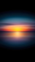 Dramatic sunset over calm water with vibrant orange and yellow hues blending into deep blue sky, creating serene atmospheric mood for backgrounds.