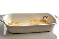 Empty white ceramic baking dish with food residue and stains after cooking, showing signs of use on white background, isolated for culinary and kitchen concepts.