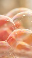 Colorful soap bubbles with water droplets floating in soft warm light creating dreamy abstract background with rainbow reflections and bokeh effect.