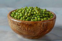 Fresh green peas in wooden bowl on marble surface, organic vegetable ingredient for healthy cooking and plant-based cuisine.