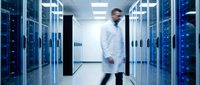 Male IT engineer in white lab coat walking through modern data center with glowing blue server racks, motion blur effect.