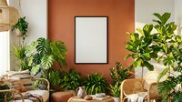 Boho living room interior with blank frame mockup on terracotta wall, surrounded by tropical plants and rattan furniture.