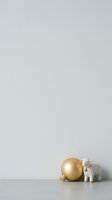 Miniature white ceramic elephant figurine standing beside large golden ornament ball on neutral surface with copy space.