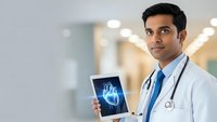Young Indian male doctor in white coat holding tablet displaying heart scan in modern hospital corridor for medical technology presentations.