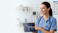 Female veterinarian in blue scrubs holding tablet with dog x-ray in modern clinic office, smiling while reviewing medical imaging for pet healthcare diagnosis.