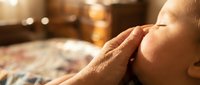 Tender moment as an adult hand gently touches a sleeping newborn's cheek in warm golden light, evoking love, care, and family bond.