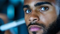 Close up portrait of young African American man with beard and intense blue eyes looking thoughtfully to side against blurred background. Modern lifestyle concept.
