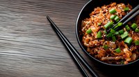 Spicy kimchi fried rice garnished with green onions and sesame seeds in black bowl on wooden table, traditional Korean cuisine served with chopsticks.
