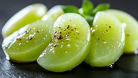 Fresh green grape slices sprinkled with black pepper on dark background, macro shot showing juicy fruit texture and seasoning detail. Perfect for culinary concepts.