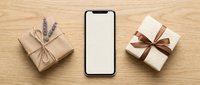 Smartphone with blank screen surrounded by wrapped gift boxes with ribbons on wooden surface for app mockup and promotional content.