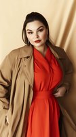 Asian woman in red wrap dress and beige trench coat poses confidently against neutral background. Professional fashion portrait showcasing plus size style and elegance.