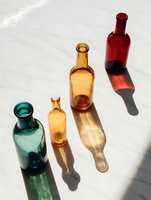 Colorful glass bottles in green, amber, and red casting long shadows on white marble surface, creating minimalist composition for food and beverage industry.