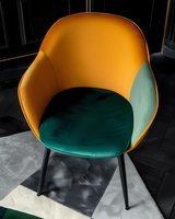 Modern armchair in mustard yellow and emerald green velvet upholstery with black metal legs on dark background, contemporary interior design element.