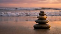 Zen stone stack on beach at sunset with golden light reflecting on wet sand and ocean waves creating peaceful meditation atmosphere for wellness concepts.