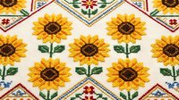 Traditional cross-stitch embroidery pattern with sunflowers and geometric borders on white fabric. Handcrafted needlework design for home decor and textile art.