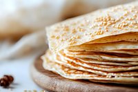 Stack of fresh homemade thin crepes or pancakes on wooden cutting board with blurred background, macro food photography with selective focus.