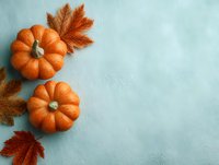 Small orange pumpkins and autumn maple leaves arranged on light blue textured background with copy space for seasonal fall designs.