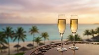 Two champagne flutes filled with golden sparkling wine on wooden table overlooking tropical beach at sunset with palm trees and ocean view for celebration.