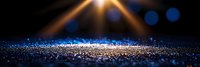 Glowing blue sparkles scattered on dark surface with bright golden light rays and bokeh effect creating magical atmosphere for festive background.