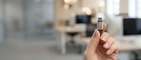 Close-up of hand holding microchip against blurred office background, representing technology innovation and digital transformation in corporate workplace settings.