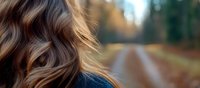 Blurred autumn forest path with woman's wavy brown hair in foreground, shallow depth of field creates dreamy atmosphere for lifestyle and beauty concepts.