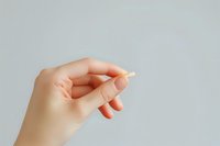 Female hand holding small yellow pill against light gray background, minimalist medical and healthcare concept composition for pharmaceutical advertising.