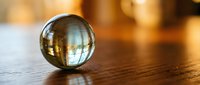 Clear glass sphere on wooden surface reflecting warm ambient light creating artistic bokeh background for meditation and mindfulness concepts.