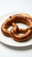 Freshly baked pretzel with coarse salt crystals on white plate, ideal for bakery, food, and culinary design projects.