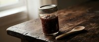 Cold brew coffee in glass jar with wooden spoon on rustic wooden surface near window, ready for morning beverage preparation and refreshment.