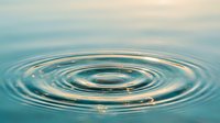 Water ripples creating concentric circles on calm surface with soft blue tones and golden light reflections for wellness and tranquility concepts.