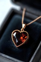 Elegant heart-shaped garnet pendant necklace in rose gold setting with detailed beaded border, displayed on dark velvet jewelry box background.
