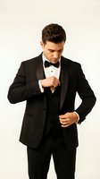 Young man with dark hair and light skin tone wearing formal black tuxedo with bow tie, adjusting jacket against white background for events, weddings, and formal occasions.