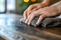Close-up of hands using microfiber cloth to clean and polish wooden surface in bright kitchen interior with natural lighting and bokeh background.