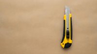 Yellow and black utility knife with retractable blade on brown cardboard background for construction and crafts projects.