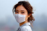 Young Asian woman wearing protective face mask looking at camera with confident expression against blurred urban background. Healthcare concept.