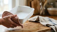 Close-up of hands holding waffle cone over wooden table with white bowl and kitchen linens, food preparation scene.