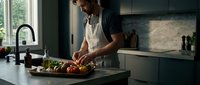Young bearded man preparing fresh vegetables on cutting board in modern kitchen with natural lighting for healthy home cooking and meal preparation.