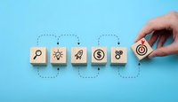 Business strategy concept with wooden blocks showing process from research to target achievement on blue background.
