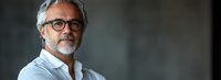 Mature Caucasian businessman with gray hair and glasses wearing white shirt against dark background, confident professional portrait with copy space.