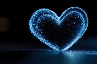 Glowing blue heart shape created from sparkling particles against dark background, magical romantic atmosphere with bokeh light effects and reflective surface.