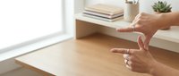 Woman hands gesturing while speaking in modern minimalist home office with books and succulent plant on wooden desk near bright window.